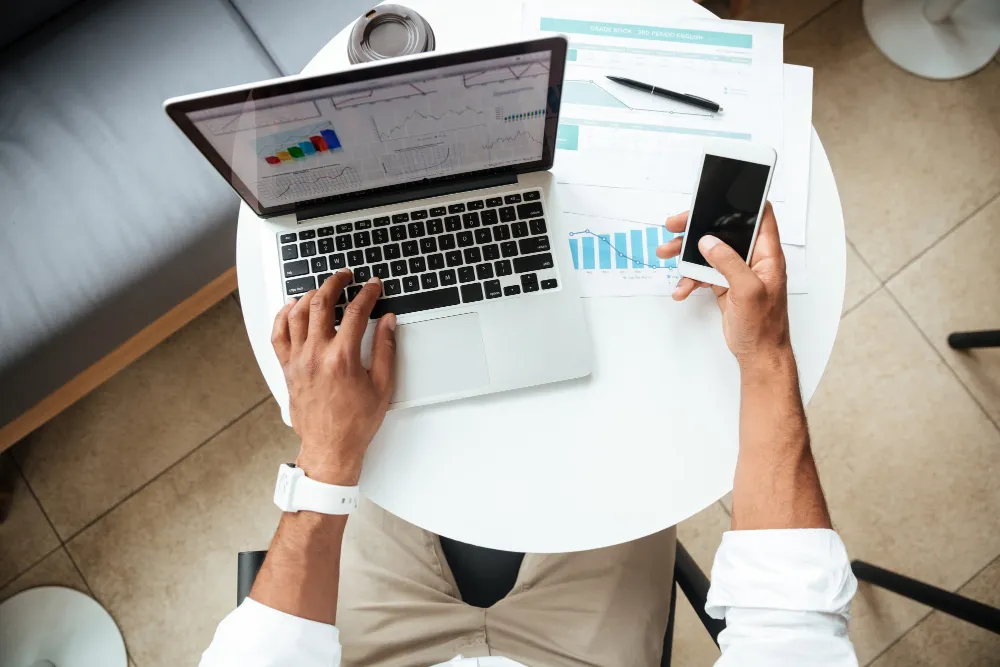 an employee is analysis and calculating digital marketing cost with his phone and laptop
